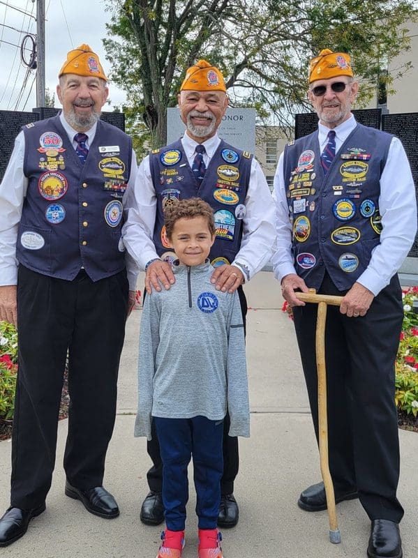 Three veterans with child at memorial site.