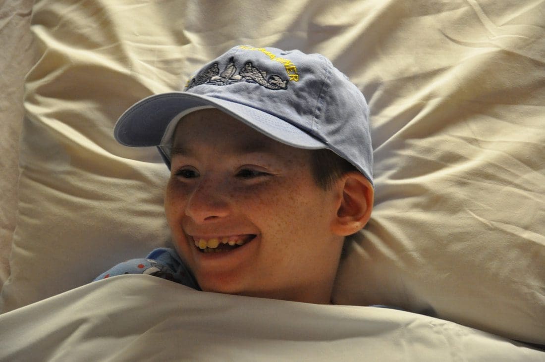 Smiling child wearing a cap in bed.