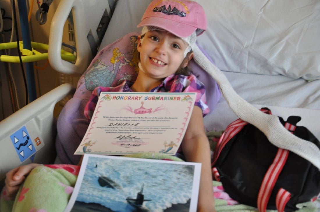 Child holding honorary submariner certificate in hospital.