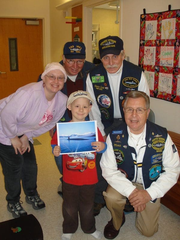Child posing with veterans and a photo.