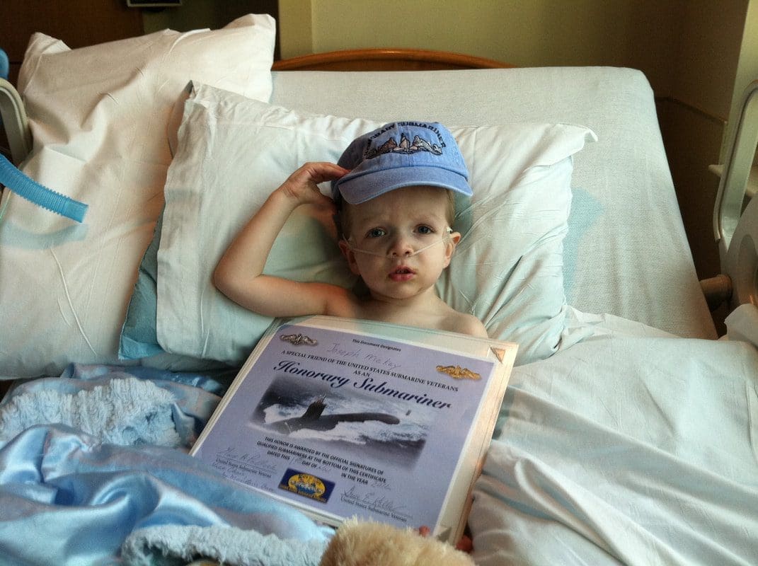 Child in bed holding honorary certificate.
