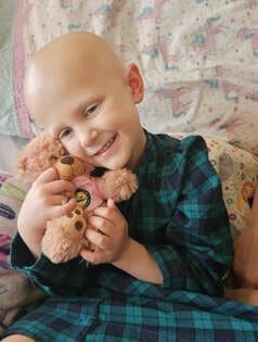 Child smiling and hugging a teddy bear.