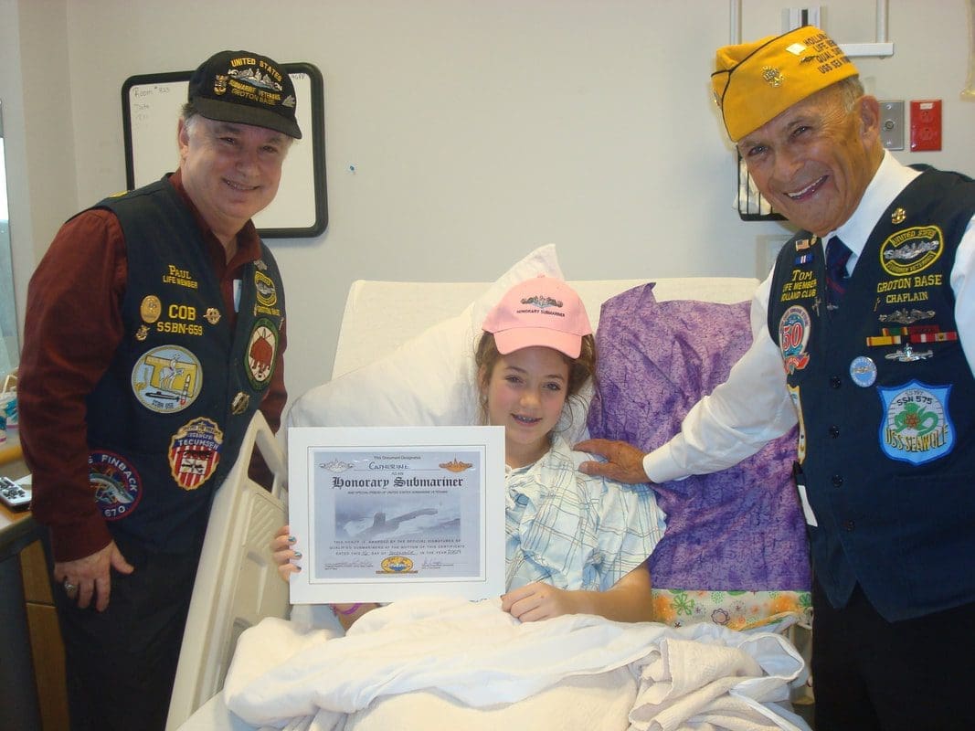 Child in hospital bed holding certificate, smiling.