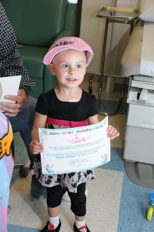 Child holding certificate, wearing pink hat.