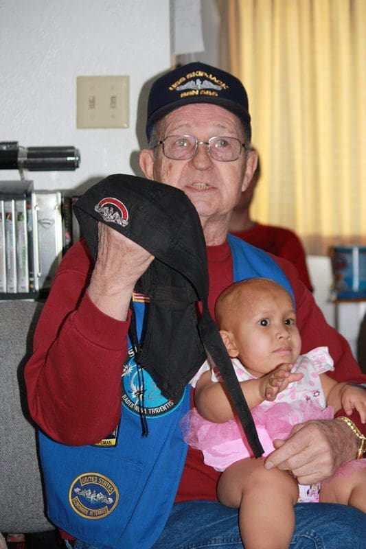 Elderly man holding a baby indoors.