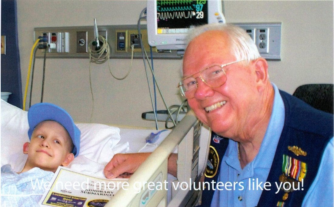 Smiling volunteer with child in hospital bed.