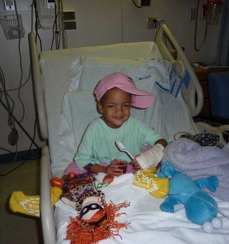 Child smiling in hospital bed with toys.