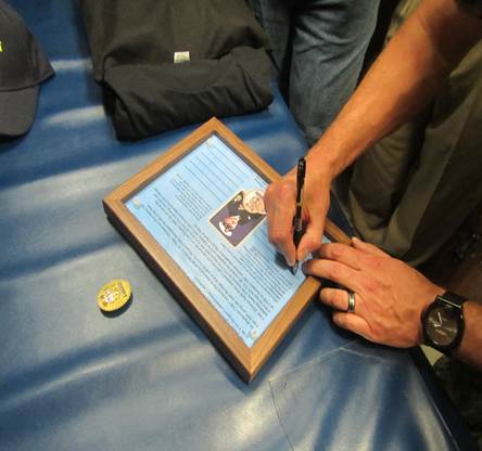 Person signing a framed certificate or document on a blue surface.